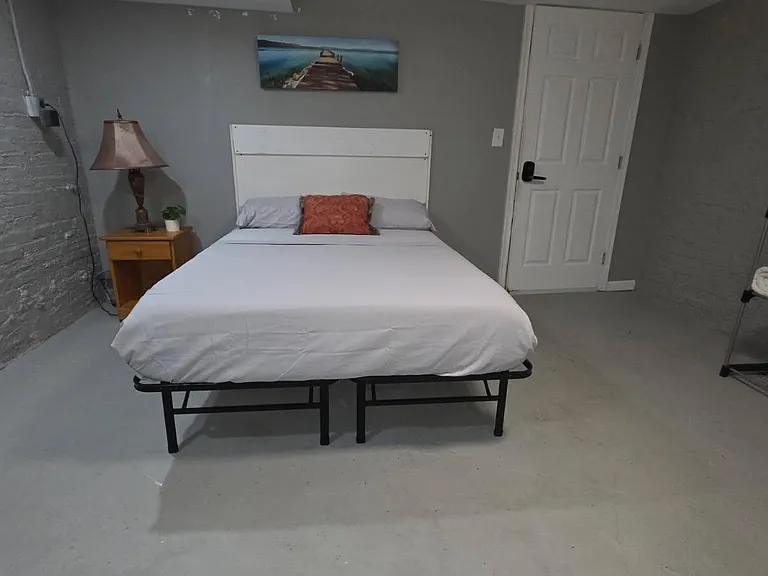 Furnished bedroom with a full-size bed, bedside table and lamp, plus open shelving for extra storage.