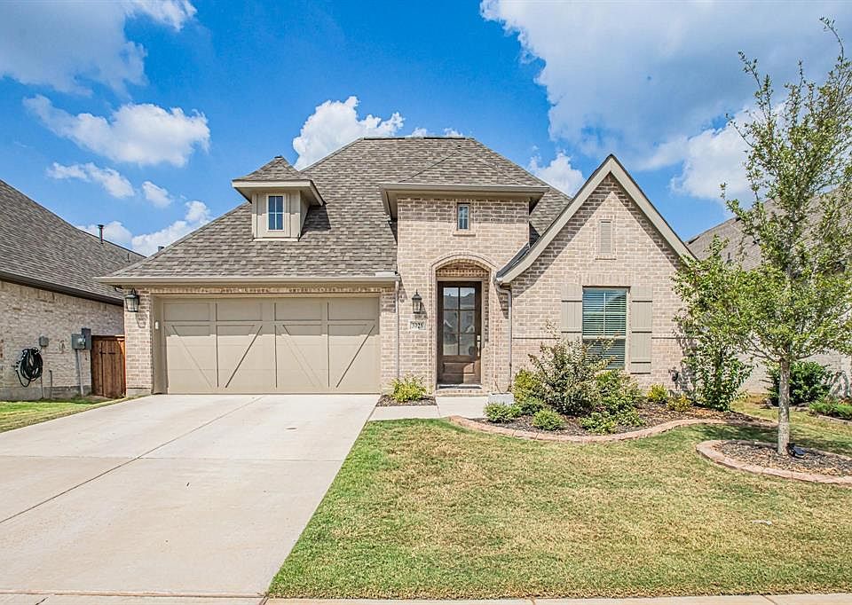 French provincial home featuring a garage, a shingled roof, concrete driveway, a front lawn, and brick siding