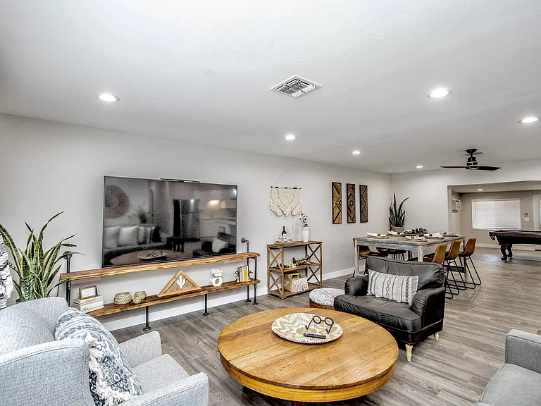 Spacious open layout at Casa Del Sol, Tempe rental home. Features a cozy living room with a large 80" smart TV, vintage coffee table, boho styling, and seamless view into the dining area and game room. Perfect for group stays in a top Tempe, AZ rental