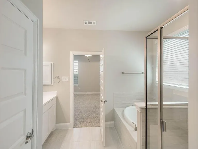 Bathroom featuring a glass-enclosed shower, a built-in soaking tub with tile surround, a single vanity with a white countertop, and light tile flooring