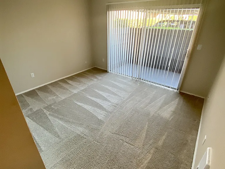 Carpeted bedroom with sliding glass door access to private porch at Villa Pacific Apartments in Oceanside, California.