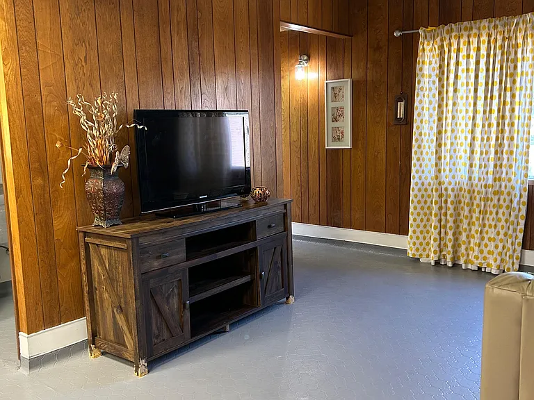 Spacious living area with wood-paneled walls, ceiling fan, and window treatments, offering flexible space for relaxing.