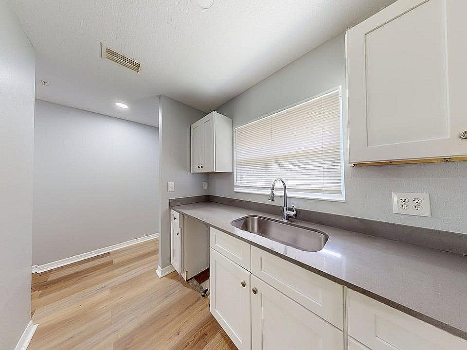 Elegant kitchen with modern gray countertops, sleek white cabinets, and warm wood flooring, offering ample natural light.