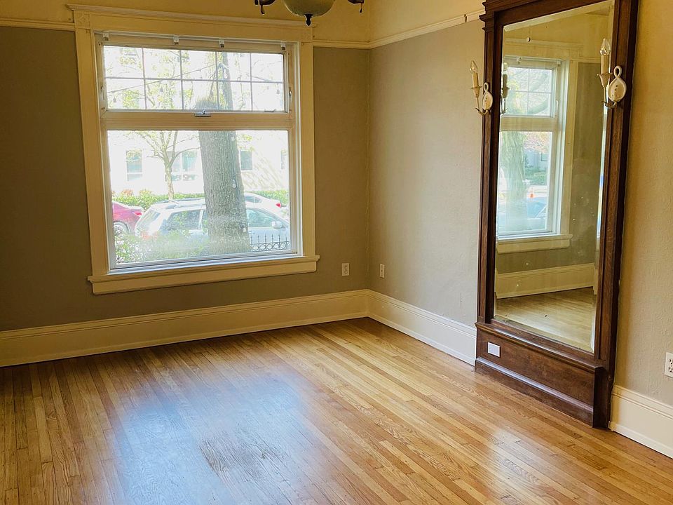 Elegant living room with hardwood floors, crown molding, large window, and unique period features.