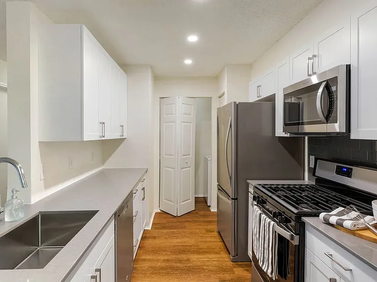 Renovated Package I kitchen with white cabinetry, grey quartz countertops, glass tile backsplash, and stainless steel appliances, and hard surface plank flooring