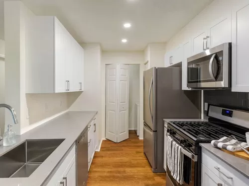 Renovated Package I kitchen with white cabinetry, grey quartz countertops, glass tile backsplash, and stainless steel appliances, and hard surface plank flooring - Avalon at Lexington