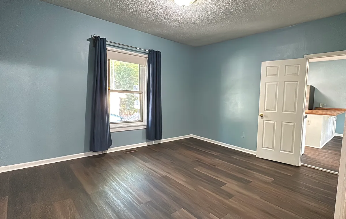 Primary bedroom with calming light blue walls, rich hardwood flooring, and ample natural light from the front window_easily fits a king-size bed and has access to an adjacent private space. - 106 N Meriah St