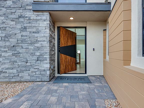 A modern and stylish entryway with a wooden and glass door, surrounded by a stone wall and a paved w