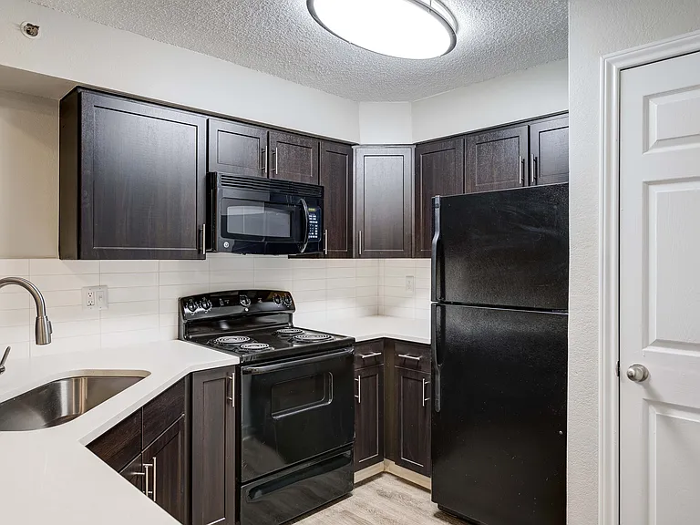 Modern kitchen with sleek dark cabinetry, black appliances, and elegant white countertops.