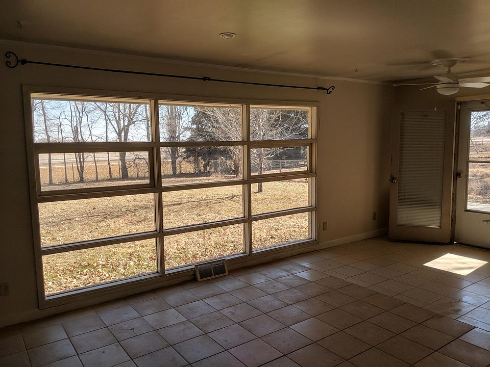 large living room window viewing fenced backyard with trees.
