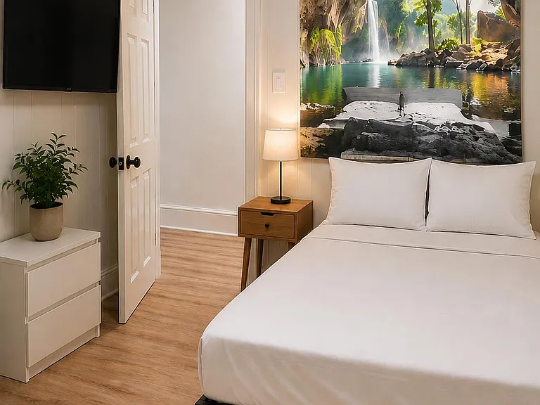Furnished bedroom with a full bed, nightstand lighting, dresser storage, and wall-mounted TV on easy-care flooring.