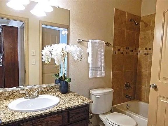 Bathroom with vanity, shower / bath combination, and a textured wall
