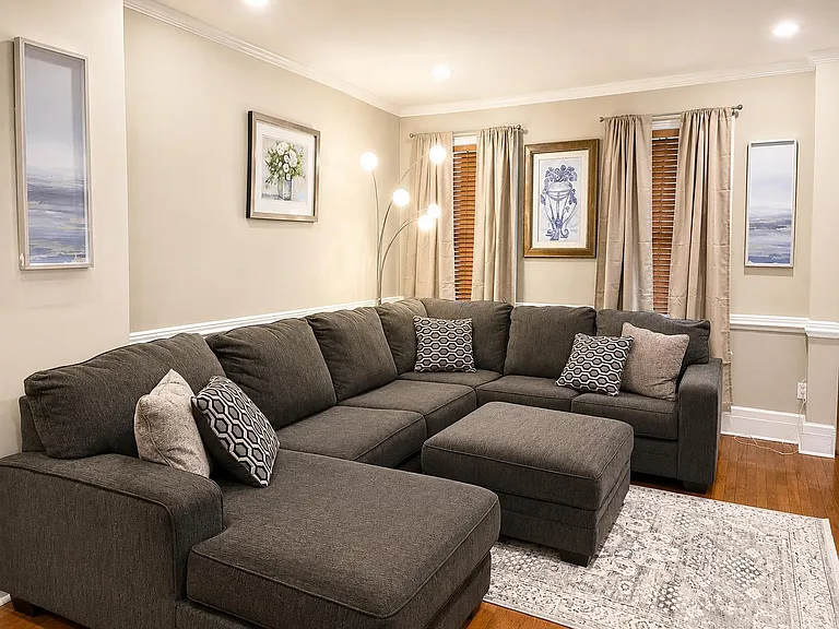 Spacious living room with a large sectional and ottoman, offering comfortable seating and natural light from multiple windows