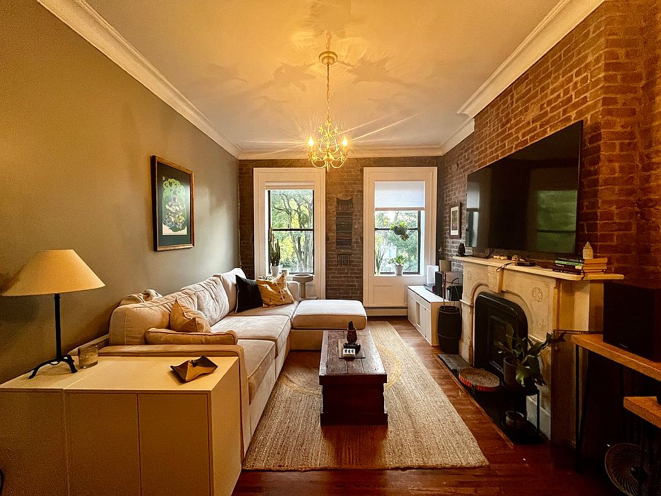 Living room - high ceilings, ornate light fixtures, hardwood floors and exposed brick adorning a decorative marble fireplace