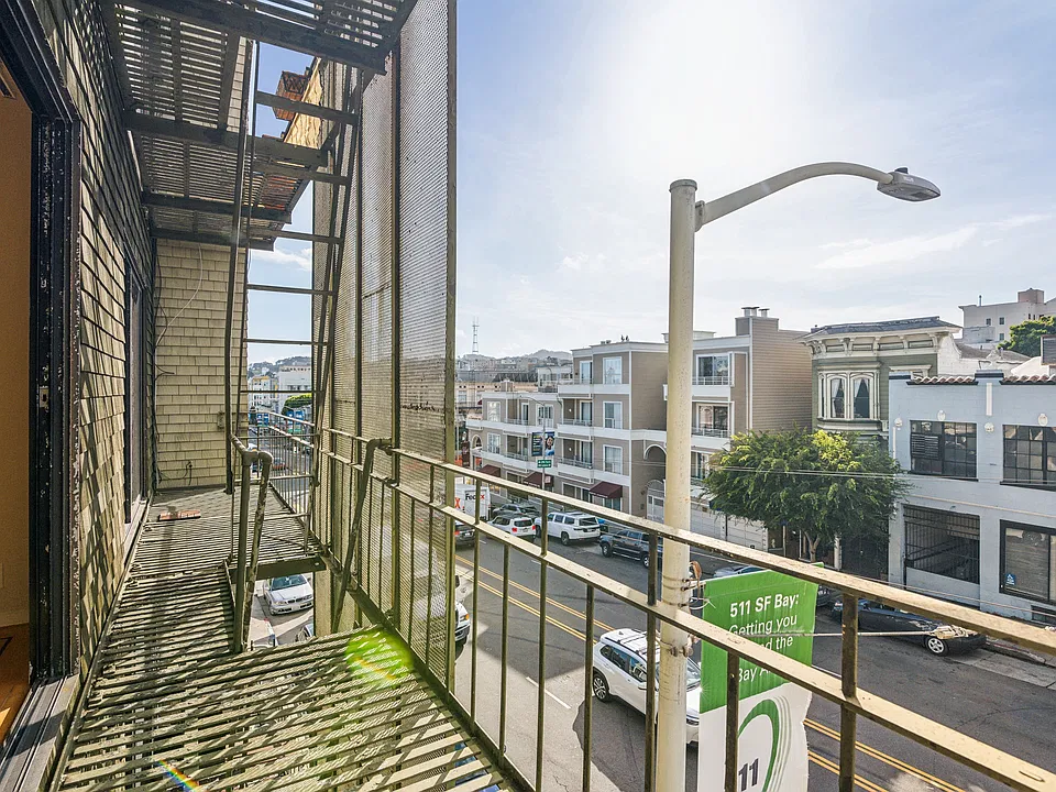 Apartment balcony overlooking a street, parked cars and with a few trees