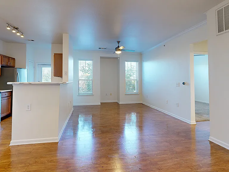 Apartment kitchen with stainless steel appliances, dining and living room with wood-style flooring.