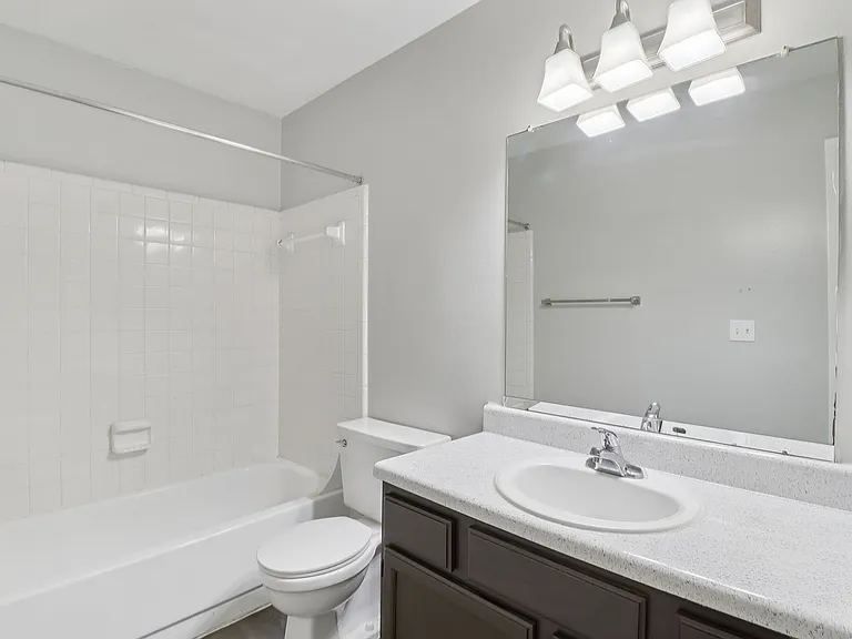 Modern and bright bathroom featuring sleek fixtures, a pristine bathtub, and a spacious vanity mirror, perfect for relaxation.