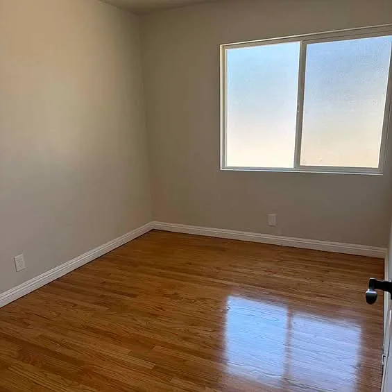Bright bedroom with refinished hardwood floors, fresh paint, and a wide window.
