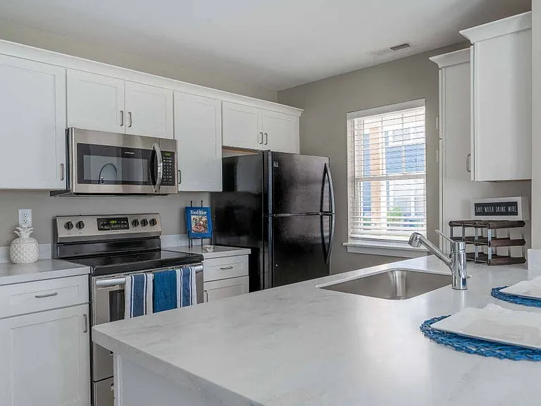 View of modern kitchen area with white shaker-style cabinetry, stainless steel appliances, and kitchen break bar