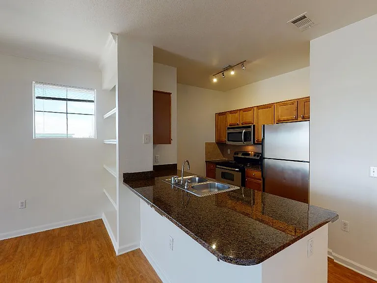 Apartment kitchen with stainless steel appliances, granite countertops and wood-style flooring.