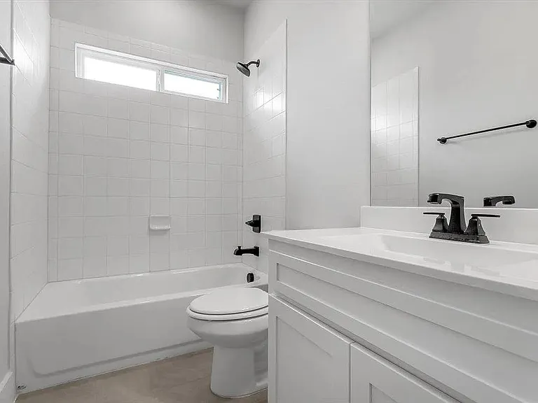Bathroom featuring a white bathtub with subway tile surround, matte black fixtures, a white vanity with integrated sink, and a horizontal transom window