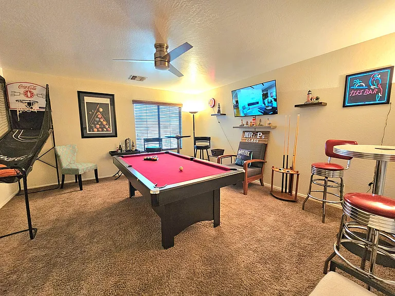 Carpeted recreation room with a pool table, wall-mounted TV, and bar-height seatingideal for entertaining and game nights.