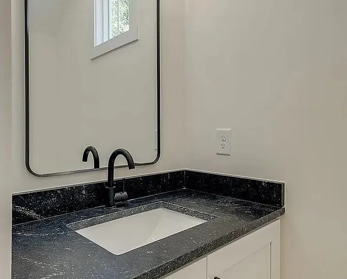 Bathroom vanity with black countertop, undermount sink, framed mirror, and window for natural light.