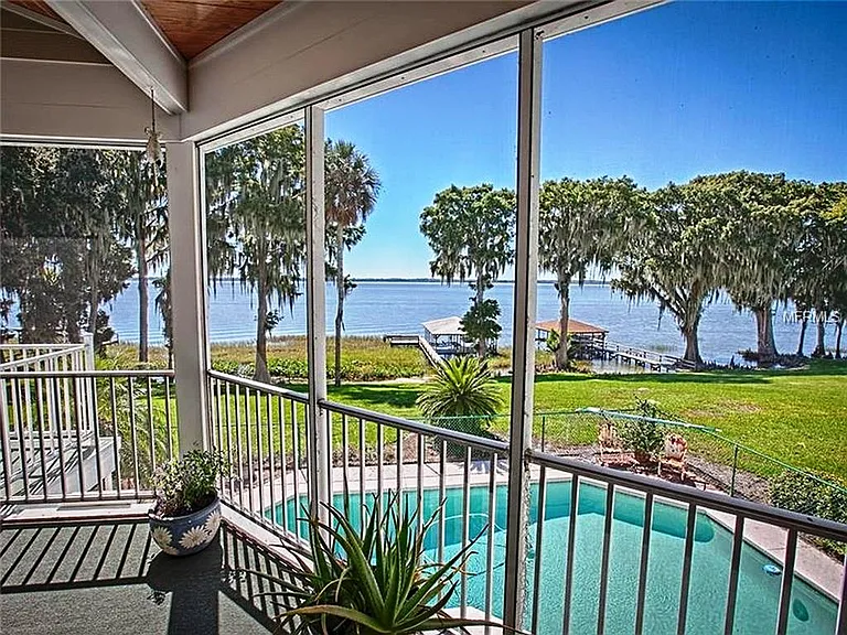 This is a view from the main screened in porch looking out to the lake, boat house and pool. The spiral staircase leads down to the pool deck and the apartment below. the flooring has been changed to a beautiful decking.