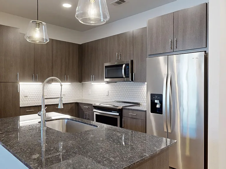 Apartment kitchen with stainless steel appliances, granite countertops, and wood-style flooring.