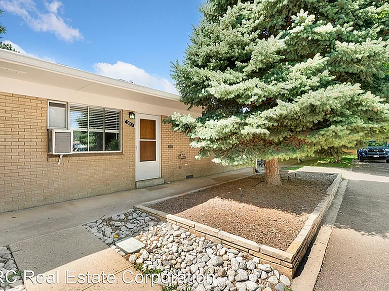 Charming single-story home with a brick exterior and front garden featuring a large, lush evergreen tree.
