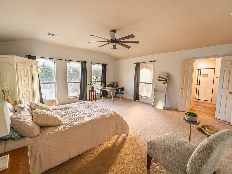 Grand Primary Suite: An exceptionally large primary bedroom retreat featuring vaulted ceilings, plush carpeting, and expansive windows. Includes a dedicated area perfect for a workspace or vanity, plus private double-door access to the en-suite bathroom.