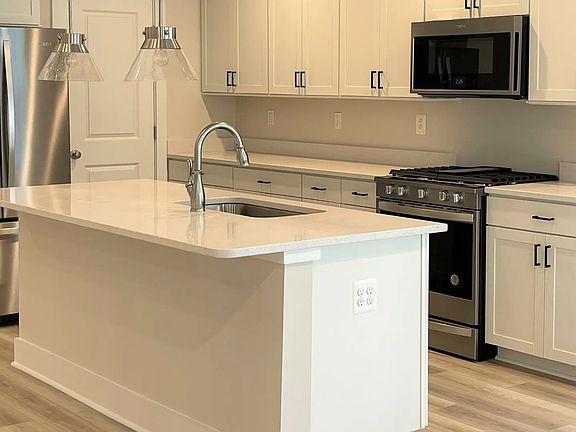 Open kitchen with large in sink island, white cabinets, white counters, and stainless steel applianc