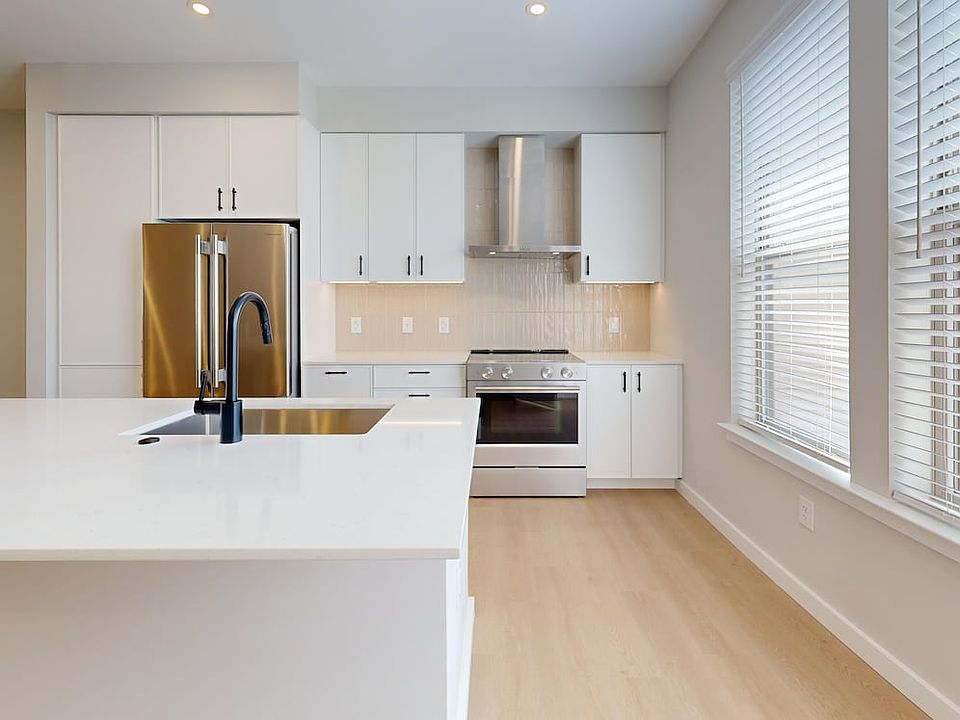 Upgrade Collection Townhome Kitchen with white cabinetry, white quartz countertops, over-the-range hood, beige tile backsplash, and stainless steel appliances