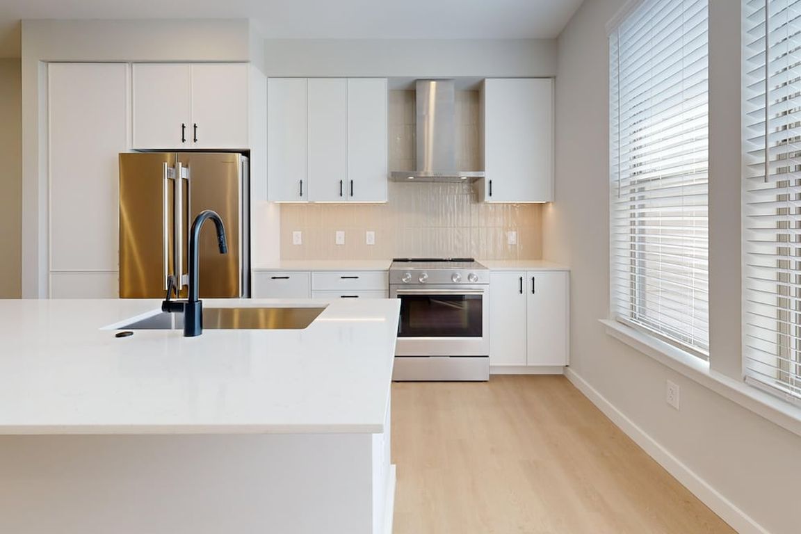 Upgrade Collection Townhome Kitchen with white cabinetry, white quartz countertops, over-the-range hood, beige tile backsplash, and stainless steel appliances