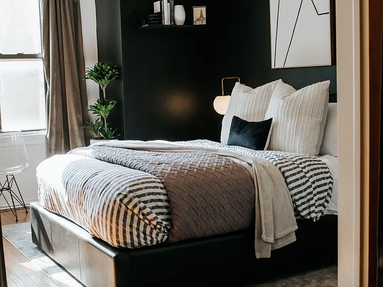 Bedroom with a queen-size bed, accent wall, and windows with drapery, plus bedside lighting and wood floors.