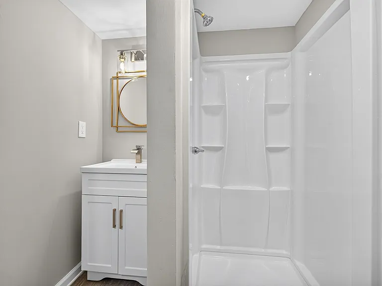 Bathroom features a white vanity with contemporary fixtures, round mirror, and a tub/shower surround with built-in shelving.