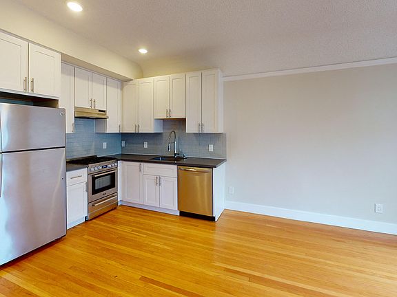 Kitchen with multiple cabinets, refrigerator, stove, range hood, and sink
