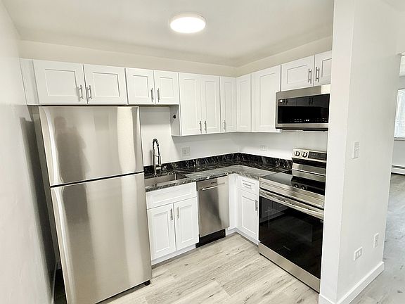 Modern kitchen with sleek stainless steel appliances, elegant white cabinetry, and a stylish black marble countertop, blending seamlessly into an open, airy layout.