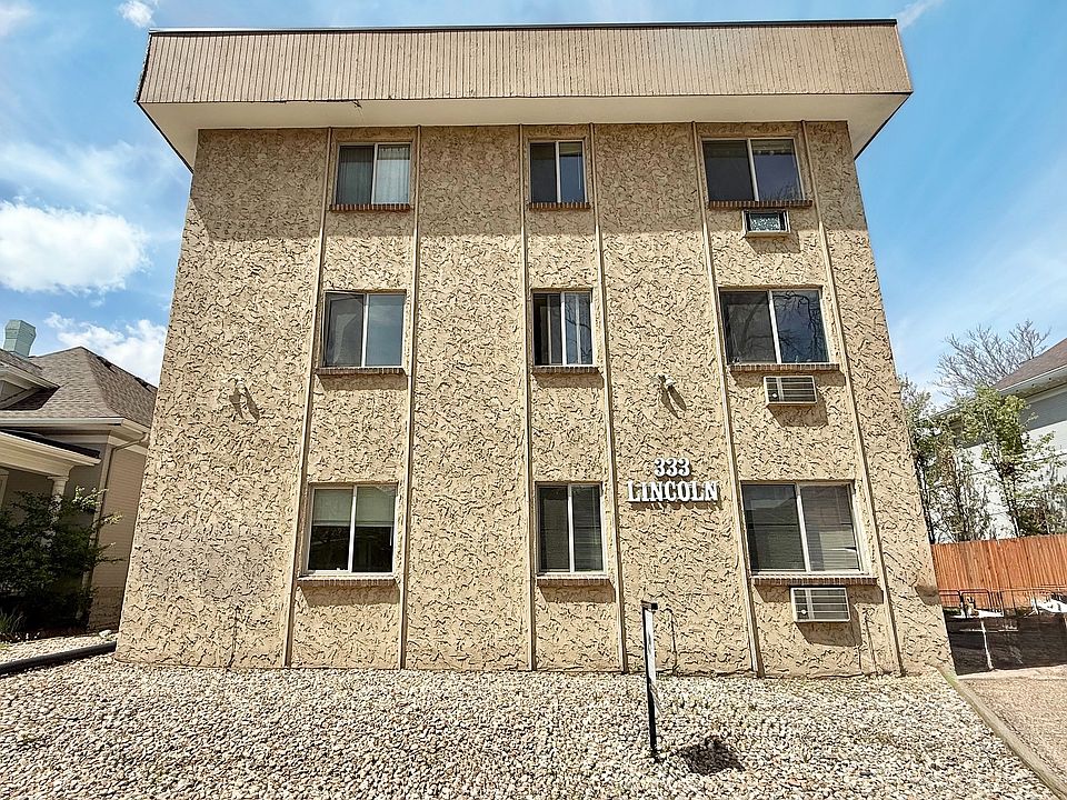 Charming three-story apartment building with textured exterior, surrounded by a neat stone landscape under a clear sky.