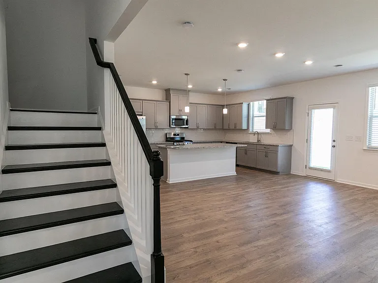 Open-concept living room with a staircase and a view into the kitchen.