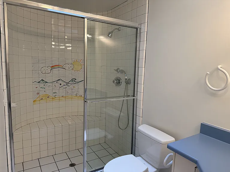 The hallway bathroom is tastefully appointed with glass shower enclosures and organized storage.