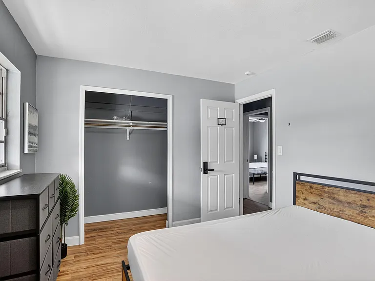 Bedroom features a large window, wood-look flooring, and an open closet plus dresser space for easy organization.