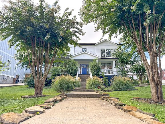 The home's inviting front entry is framed by a generous lawn, mature trees, and a landscaped pathway leading up to the front steps. A wide frontage and lush greenery add curb appeal and a warm welcome.