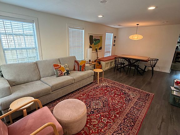 Bright, open living and dining space with abundant natural light and dark wood-look flooring.