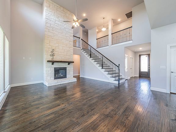 Unfurnished living room with a stone fireplace, dark hardwood / wood-style floors, ceiling fan, and a high ceiling