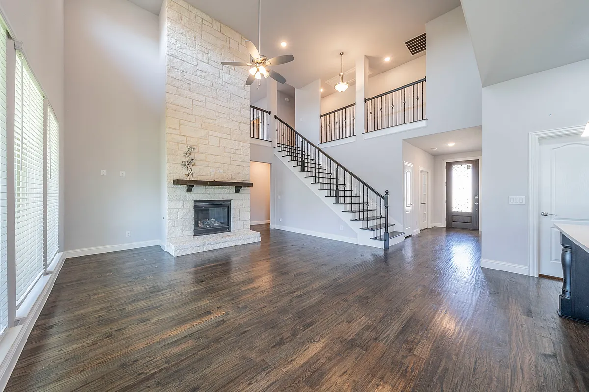 Unfurnished living room with a stone fireplace, dark hardwood / wood-style floors, ceiling fan, and a high ceiling - 9489 Autumn Glen Dr