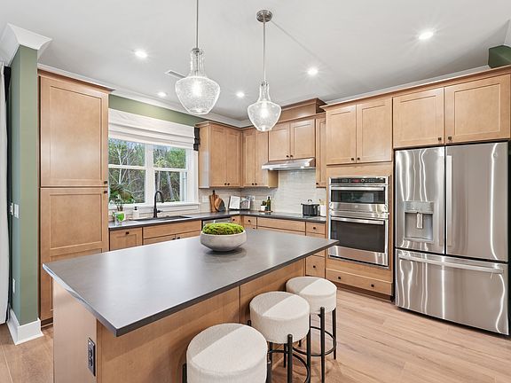 A modern, well-equipped kitchen with light wood cabinets, stainless steel appliances, and a central