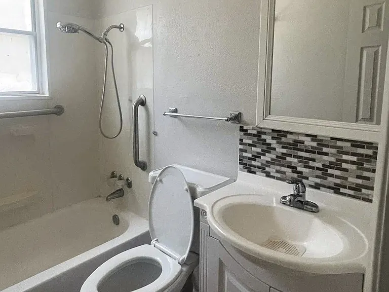Convenient full bathroom located off the main hallway, featuring a modern vanity, updated tile backsplash, and wood flooring.