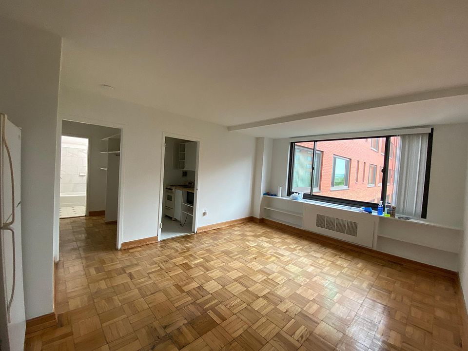 Overview of unfurnished apartment. Closet leads to bathroom; 2nd door is kitchen. Refrigerator is on left.
