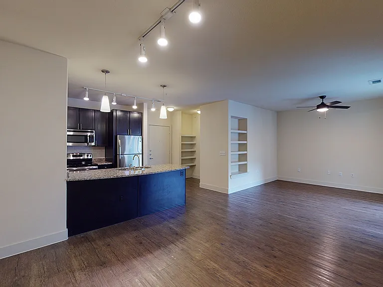 Apartment kitchen with stainless steel appliances in select homes, dining and living room with wood-style flooring.